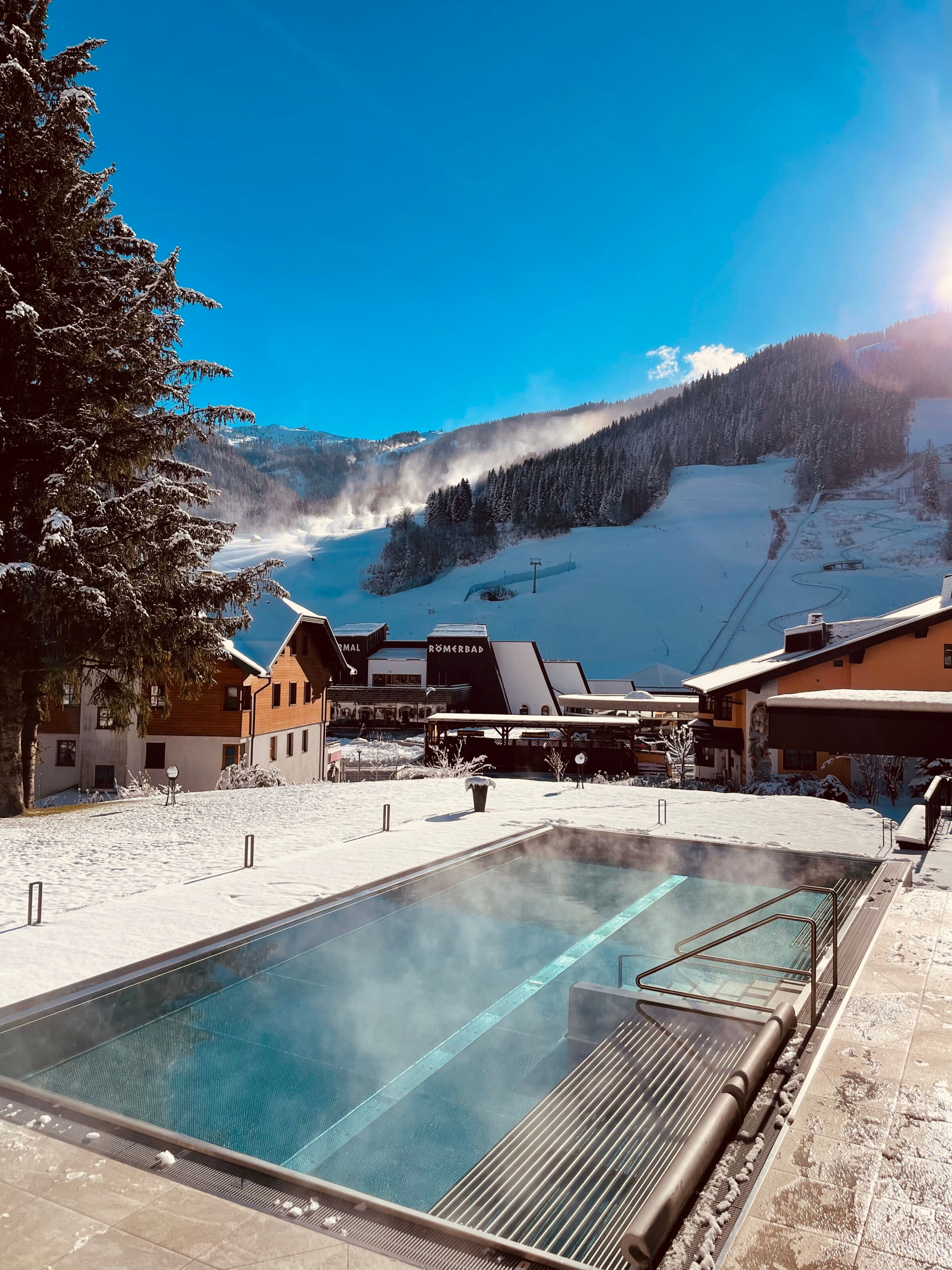 Außenpool mit schneebedecktem Boden und Bergen im Hintergrund unter klarem Himmel