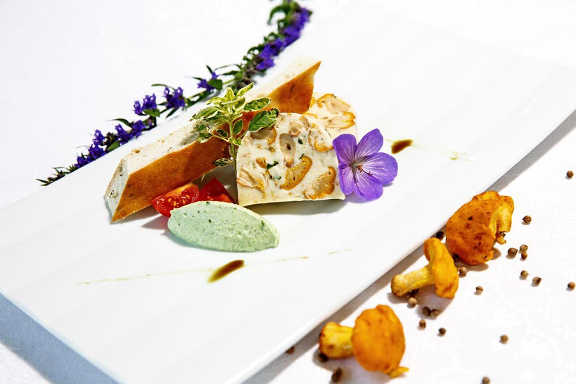 Elegantes Gericht mit Pilzen, grüner Sauce und essbaren Blüten, kunstvoll angerichtet.