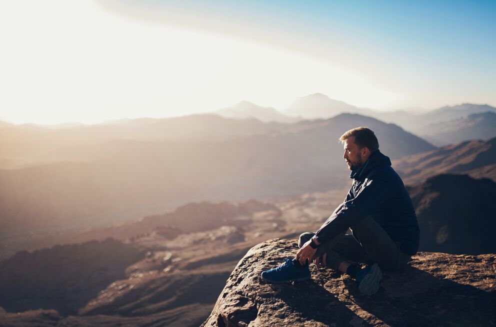 Mann sitzt auf einem Felsen und blickt über die Berge im Sonnenuntergang für entspannende Atmosphäre