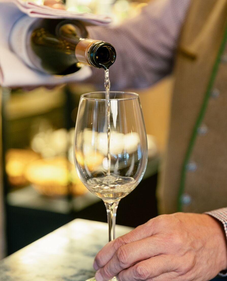 Eine Hand gießt ein Getränk in ein Glas, symbolisiert Entspannung und Luxus im Spa-Bereich.
