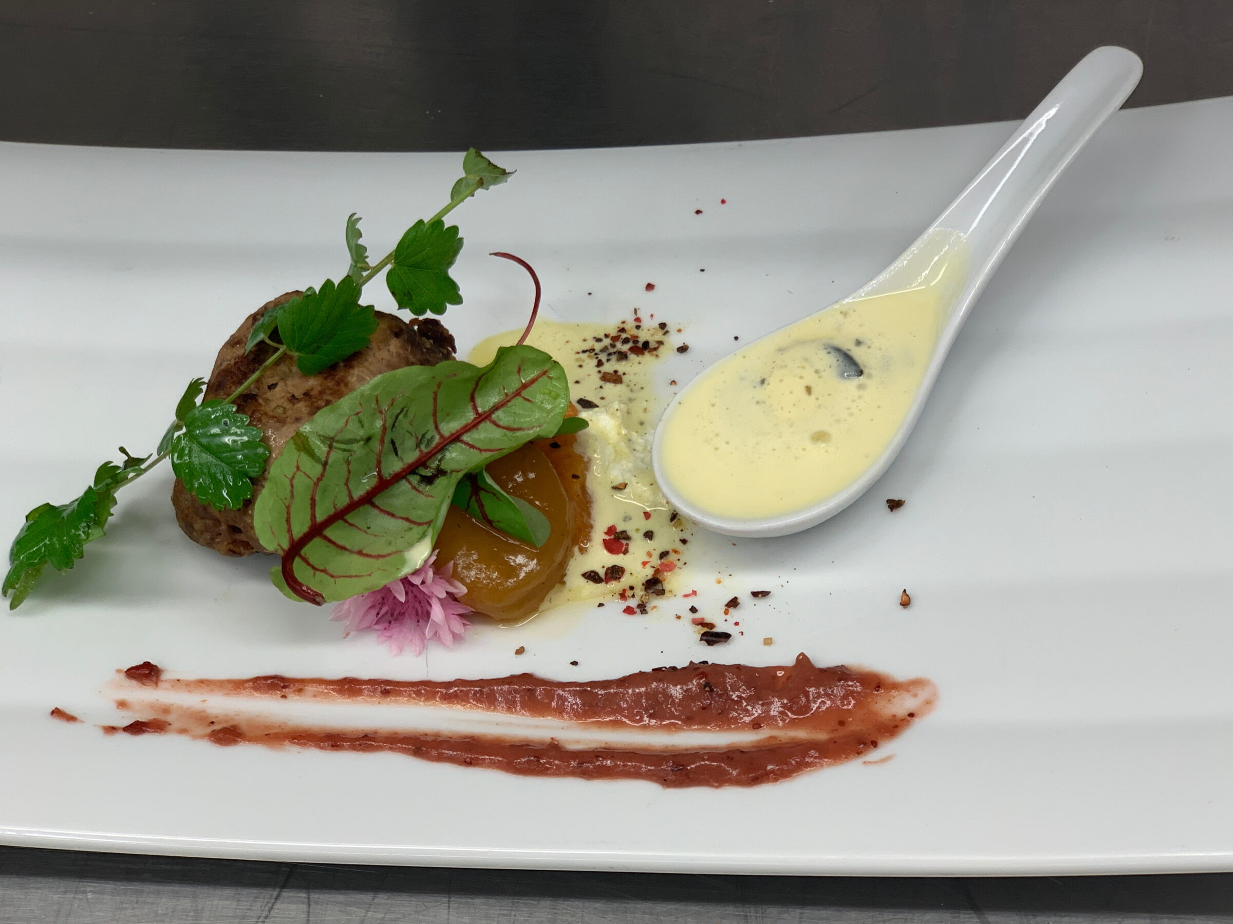 Gourmetgericht auf einem weißen Teller mit kunstvoll arrangiertem Essen und einer Sauce in einem Löffel.