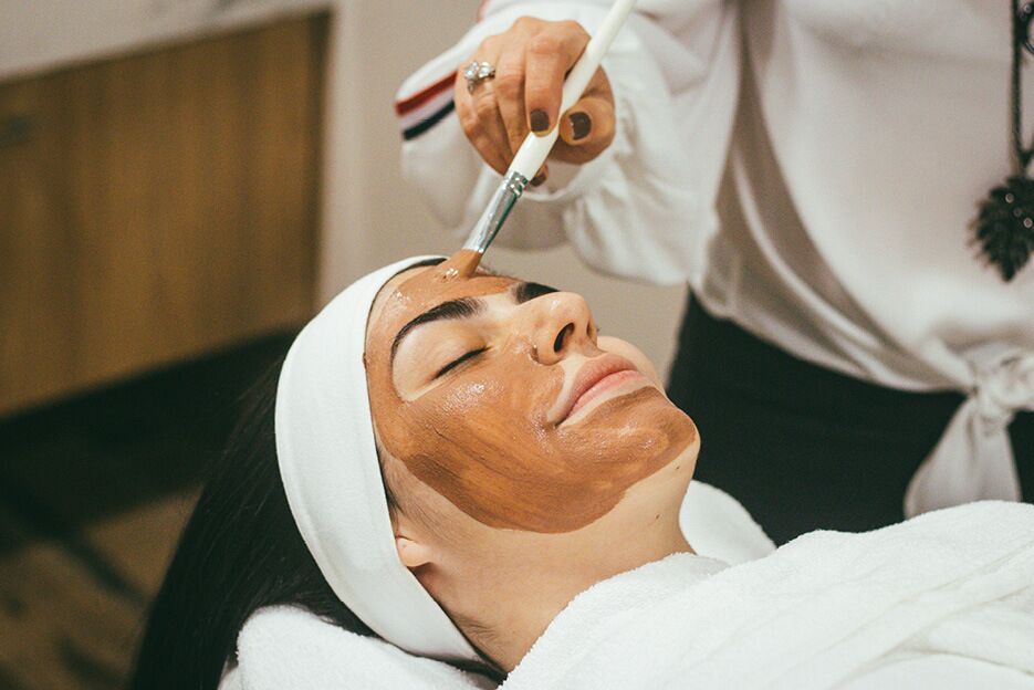 Eine Frau erhält eine Gesichtsanwendung mit einer Maske von einer Therapeutin aufgetragen.