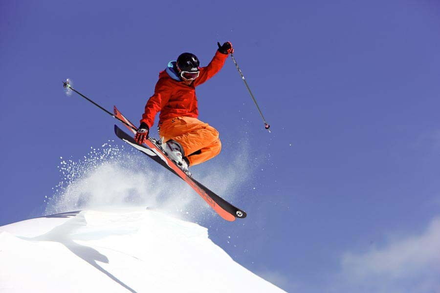 Skifahrer springt über einen schneebedeckten Hang unter blauem Himmel in Bad Kleinkirchheim