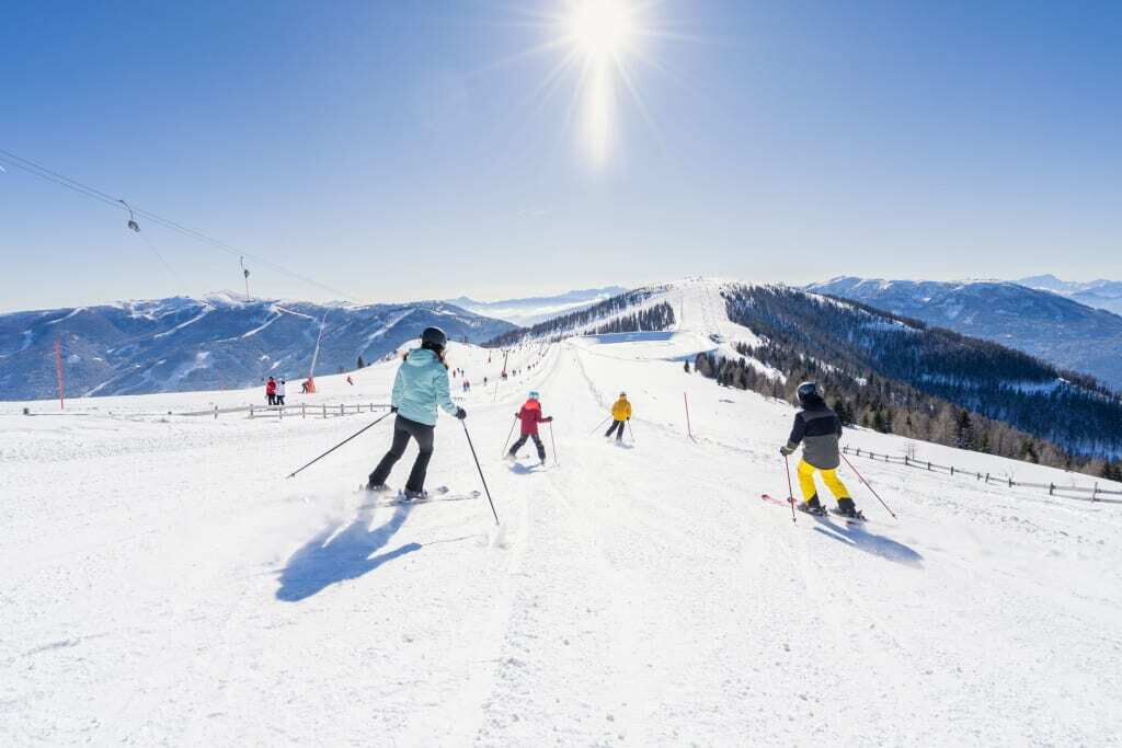 Skifahrer fahren einen schneebedeckten Hang mit Bergen im Hintergrund unter klarem Himmel