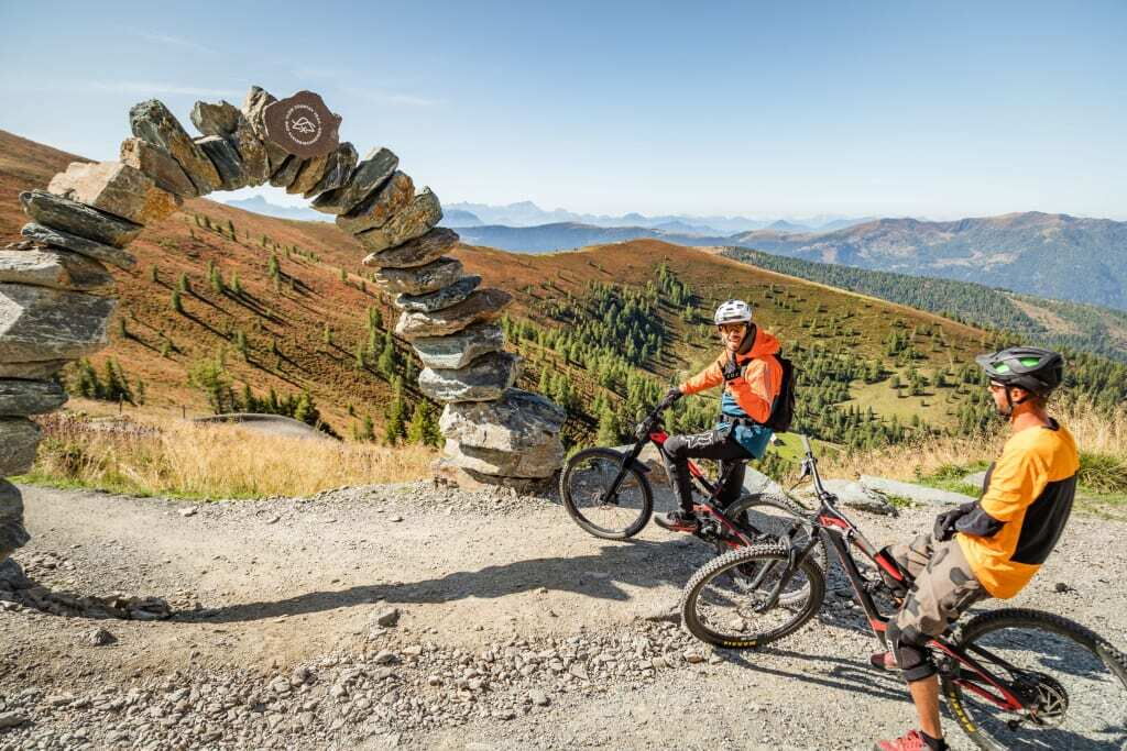 Zwei Mountainbiker machen eine Pause an einem Steinbogen auf einem Wanderweg in den Bergen.