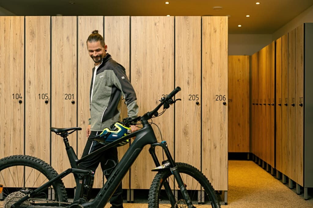 Lächelnde Person neben Mountainbike vor Holzschließfächern im Freien für Sportler