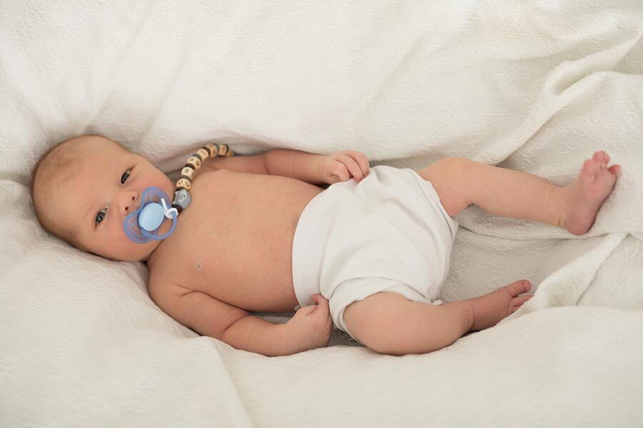 Il bambino Christian sdraiato su una coperta con un ciuccio blu in bocca.