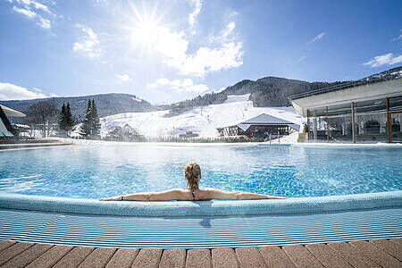 Person entspannt im Außenpool mit Blick auf die Berge unter klarem Himmel in Bad Kleinkirchheim.