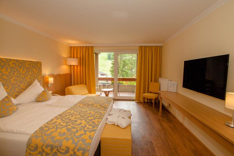 Elegantes Spa Zimmer mit großem Bett und Sitzbereich, viel Tageslicht durch große Fenster