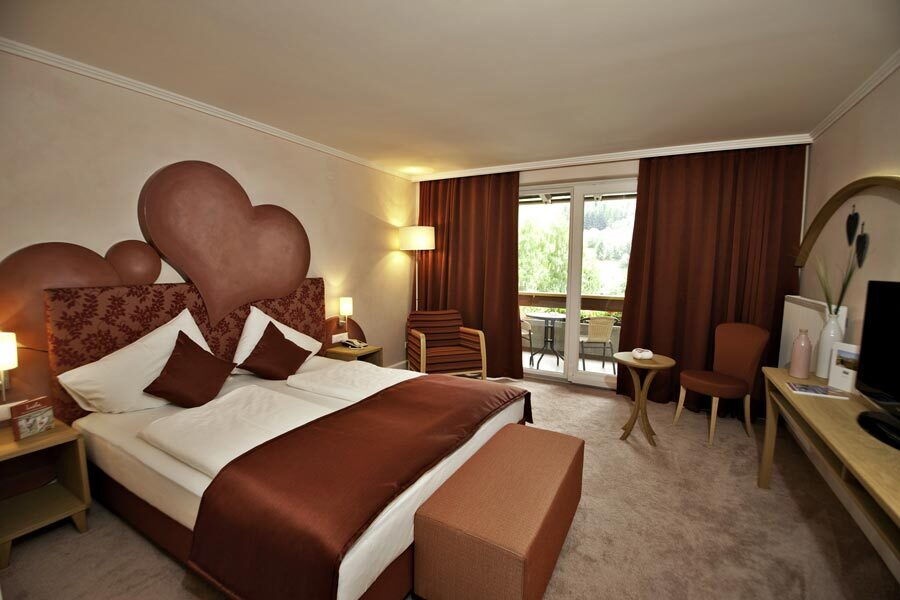 Elegante Spa-Zimmer mit Doppelbett und Sitzbereich im Wellnesshotel Prägant, große Fenster bieten Aussicht.