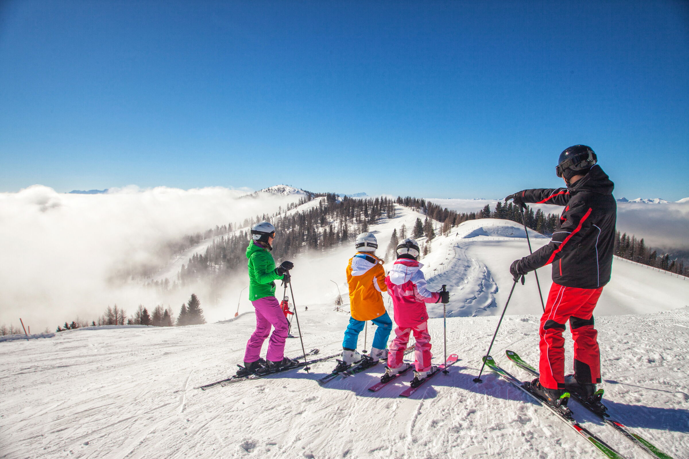 Eine Familie beim Skifahren auf einer verschneiten Piste mit einem Skilehrer im Hintergrund