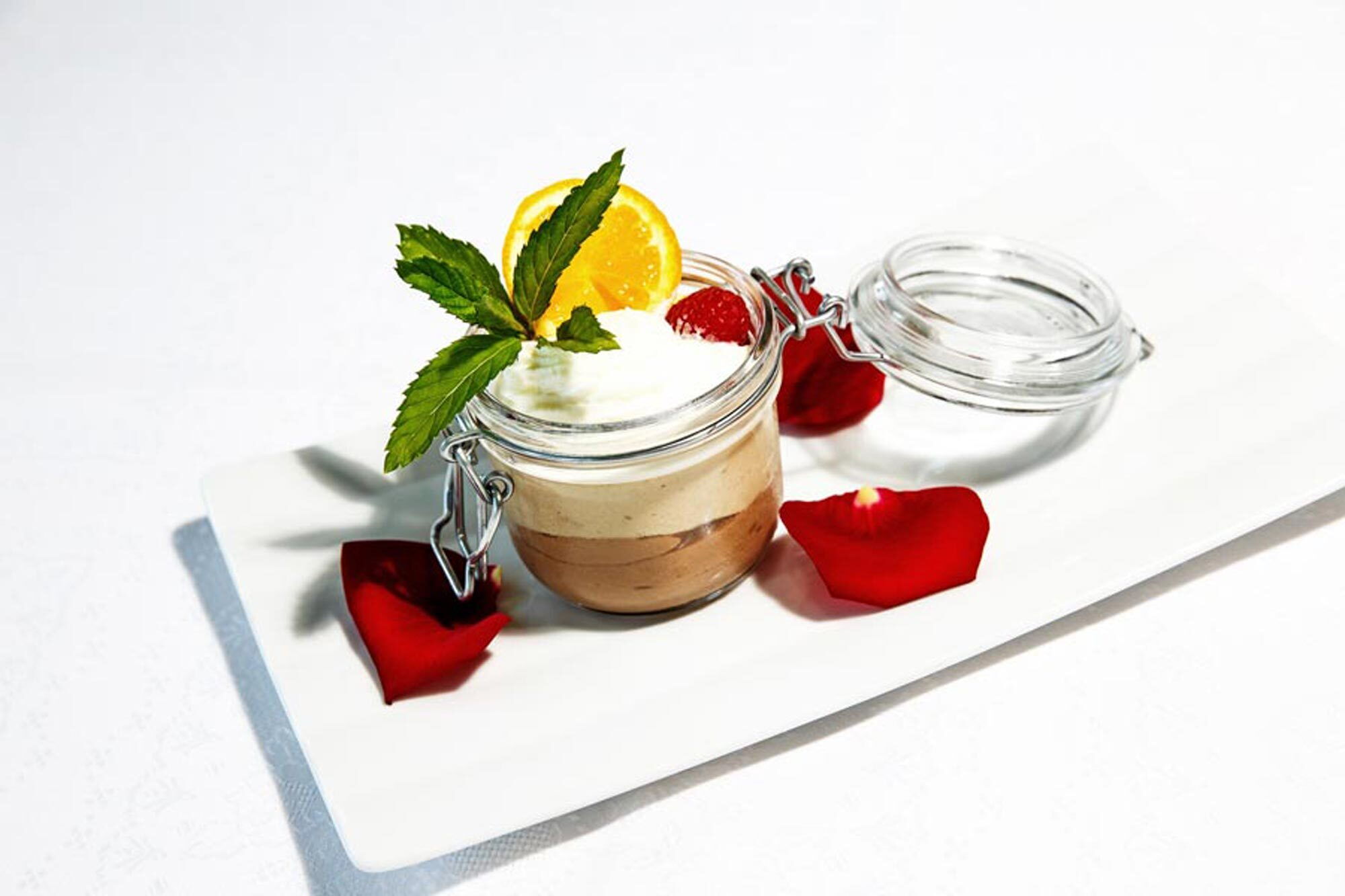 Dessert in einem Glas mit Orange, Erdbeere und Minze auf einem weißen Teller arrangiert