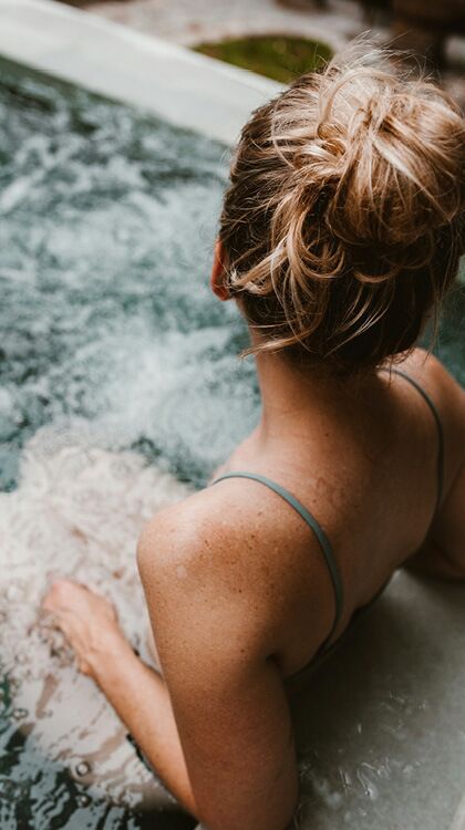 Person mit Haarknoten entspannt in einem Whirlpool umgeben von Wasserblasen bei einem Wellnessaufenthalt