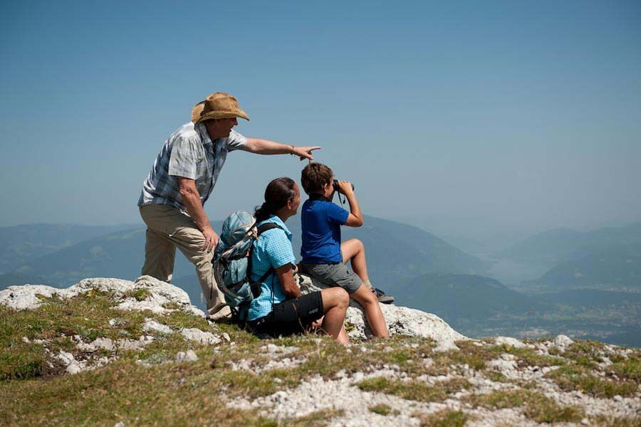 Gruppe sitzt auf Felsen und betrachtet die Landschaft, während ein Erwachsener auf etwas zeigt.