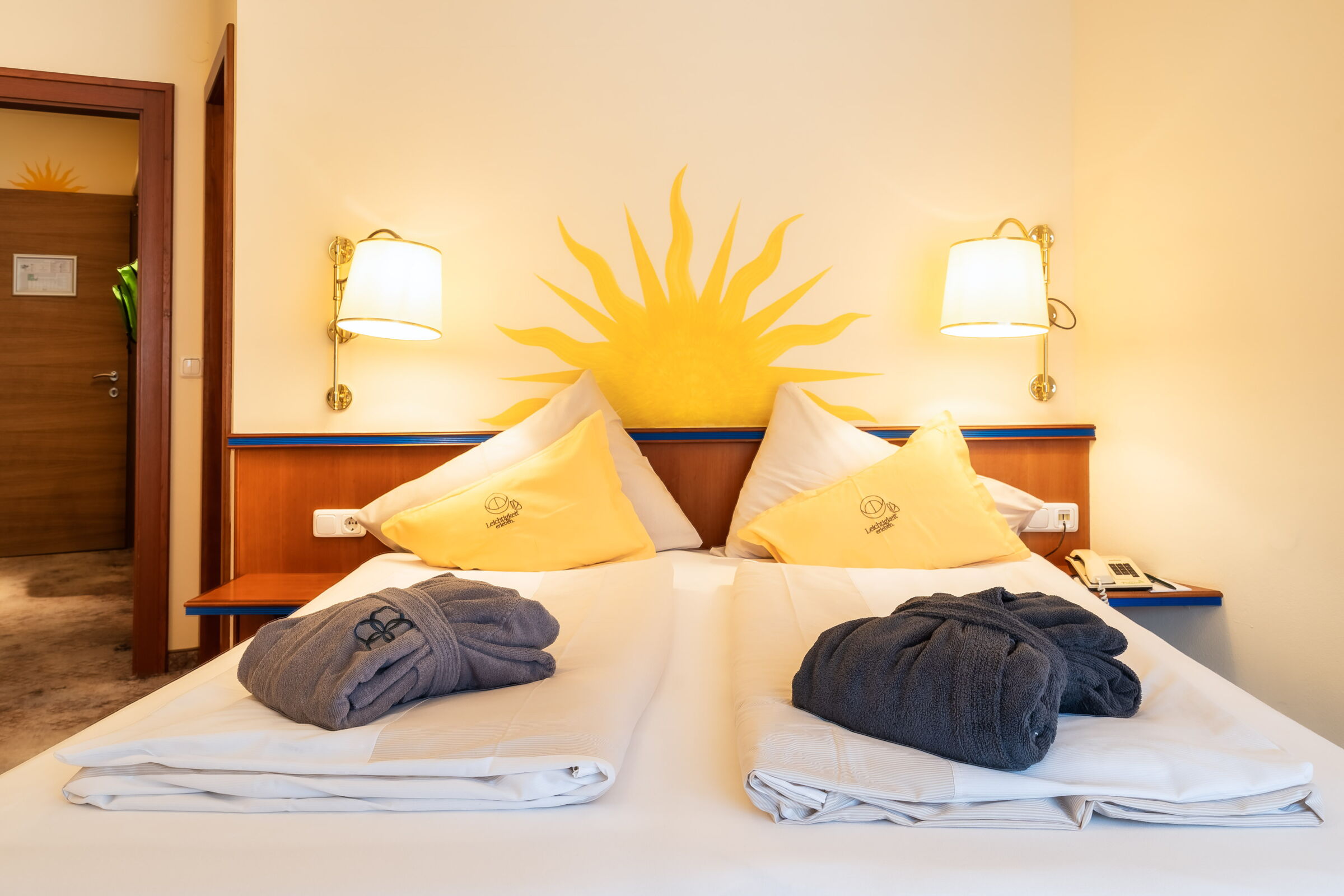 Spa-Raum mit zwei Betten, Dekokissen und Bademänteln bei warmem Licht im Wellnesshotel