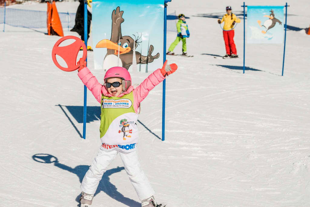 Ein Kind feiert auf einer schneebedeckten Piste mit Skihelm und Wintersportkleidung.