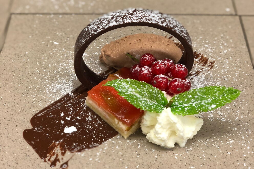 Elegantes Dessert mit Schichten aus Fruchtgelee und Schokoladenmousse, verziert mit Minze und Sahne.