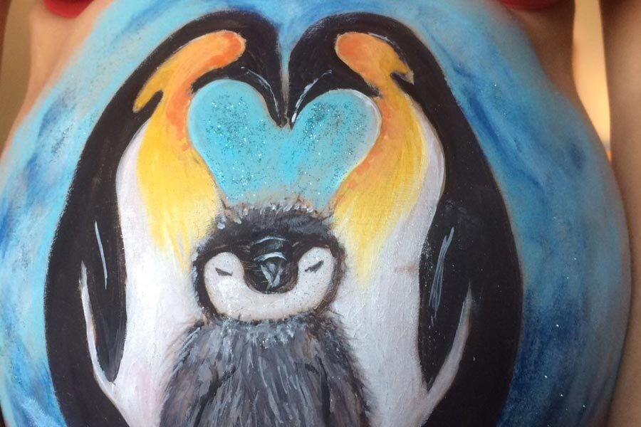 Ein Babybauch auf den eine Pinguinfamilie gemalt wurde.