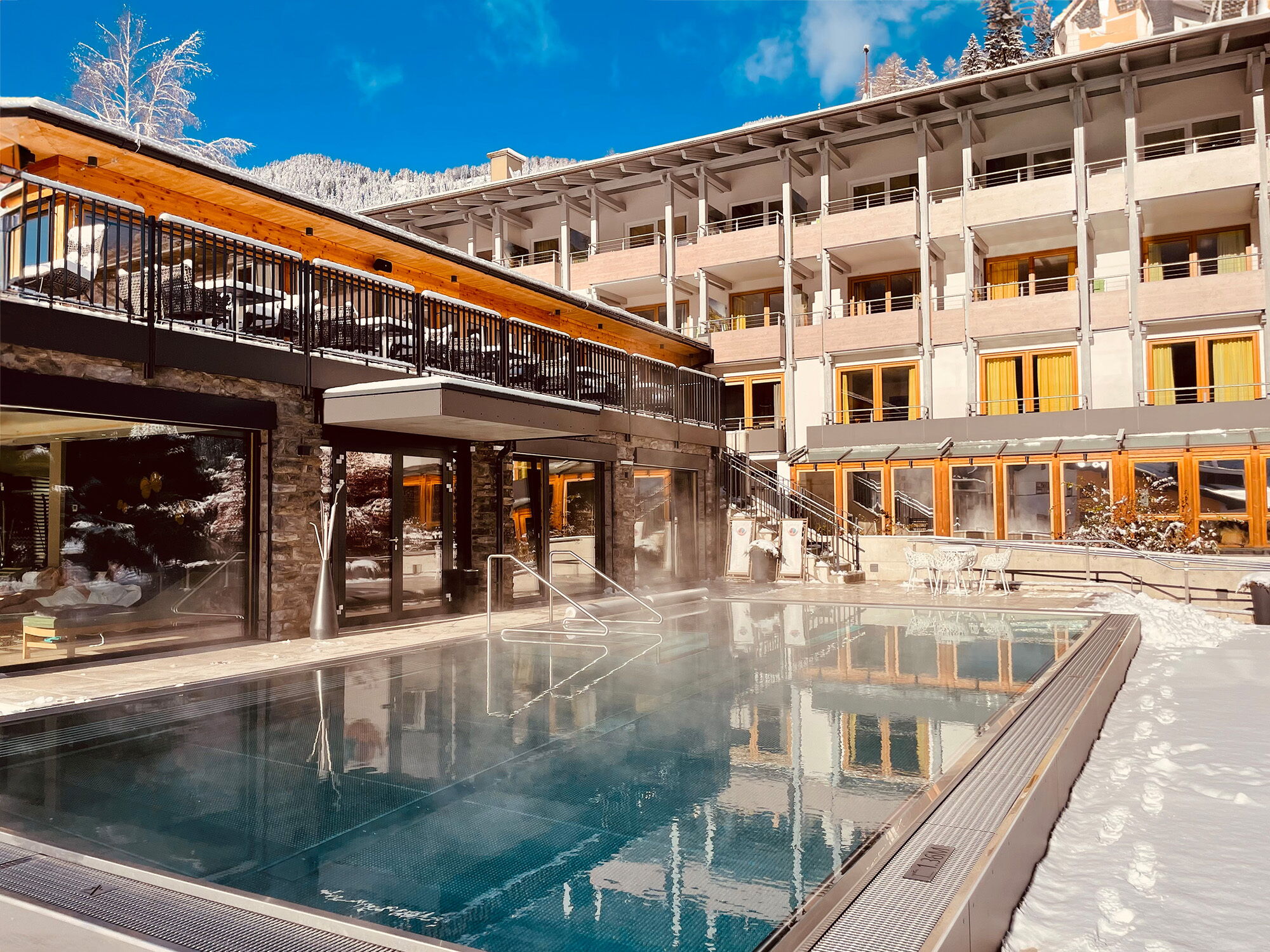 Luxuriöses Hotel mit Außenpool in verschneiter Winterlandschaft und Bergpanorama