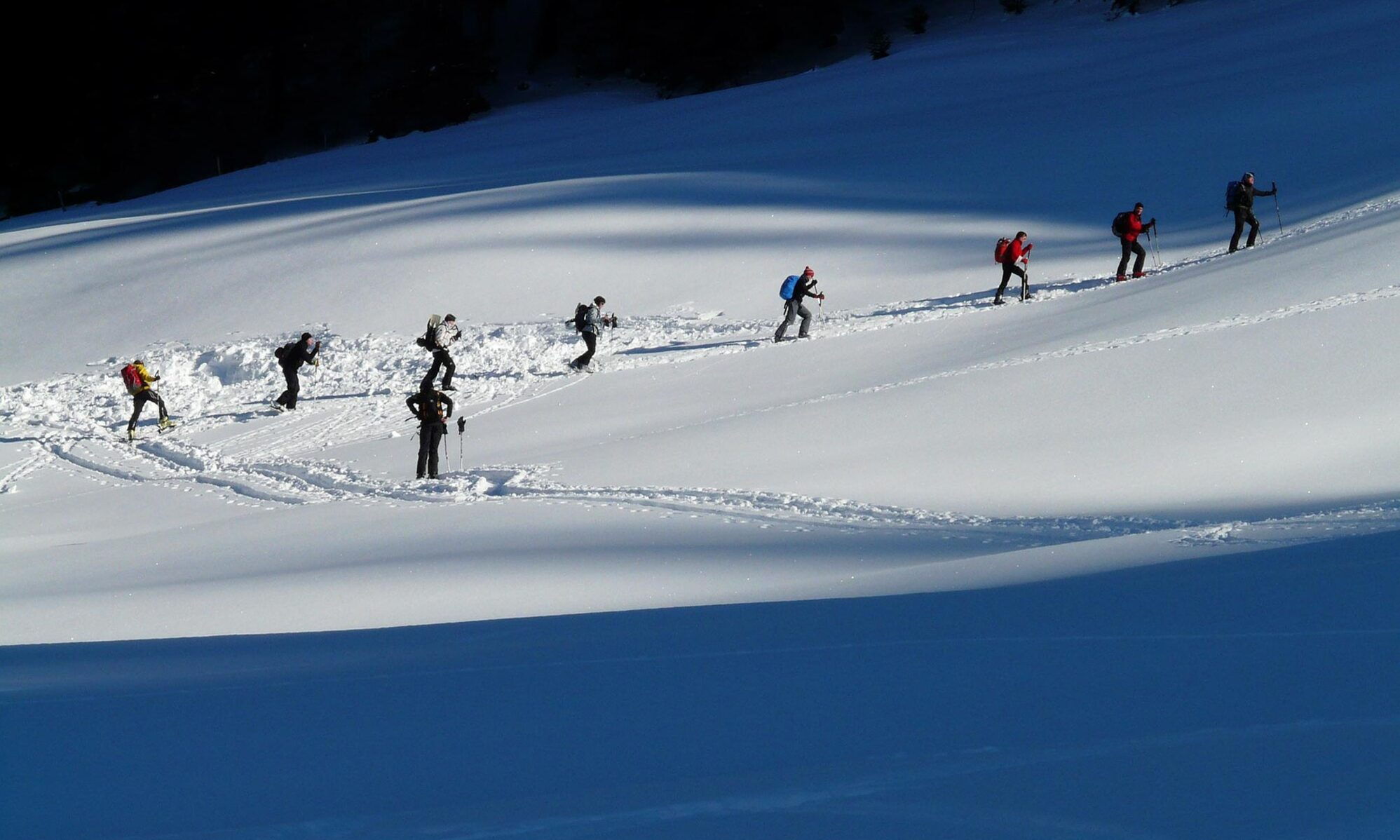 Gruppe von Menschen beim Wandern in schneebedeckter Berglandschaft über verschneiten Weg.