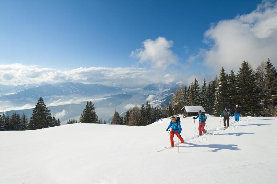 Gruppe von Personen beim Wandern durch eine verschneite Landschaft mit Bergen im Hintergrund unter blauem Himmel