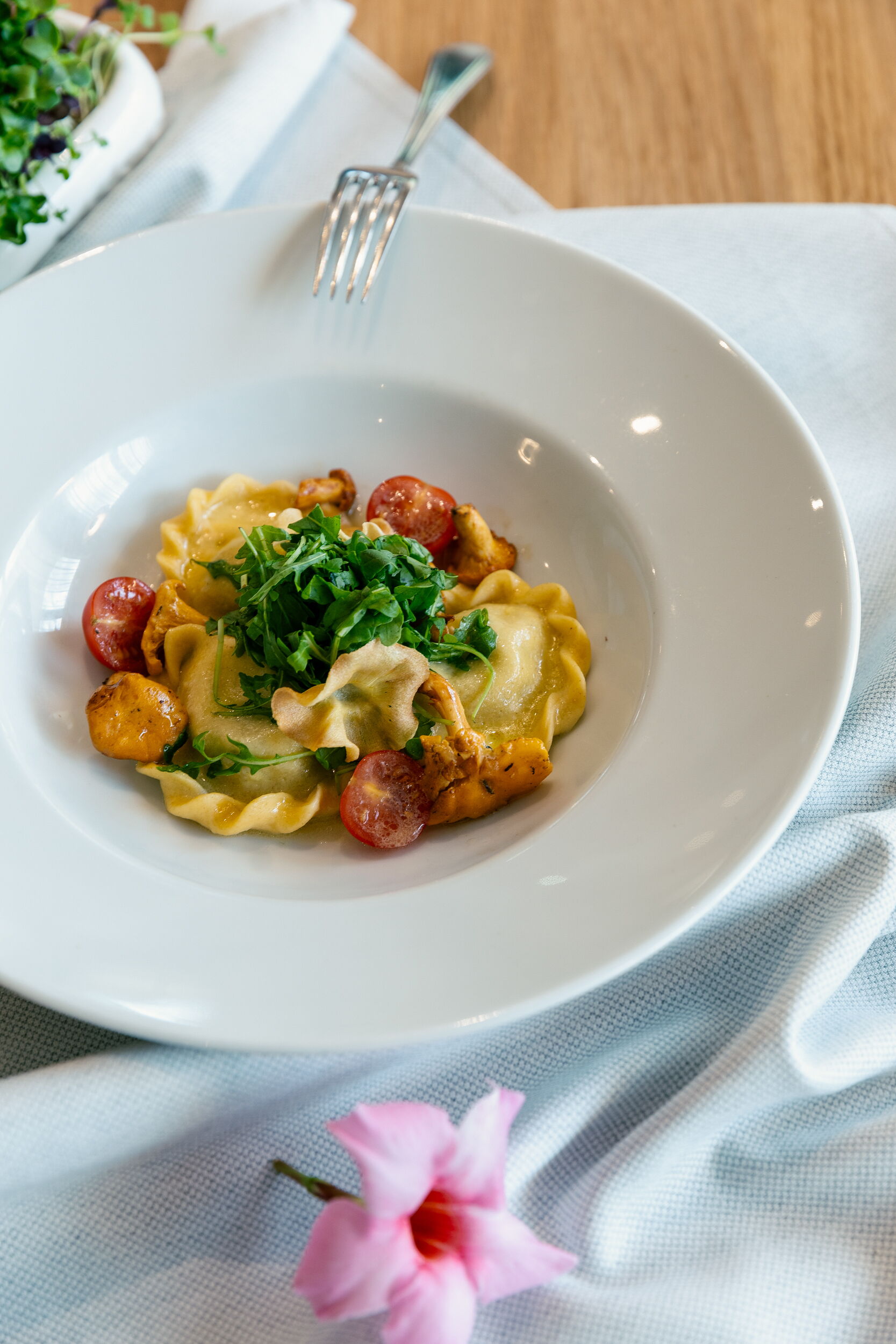 Ravioli mit Kirschtomaten und Rucola in einer weißen Schüssel, dekorative Blume im Vordergrund