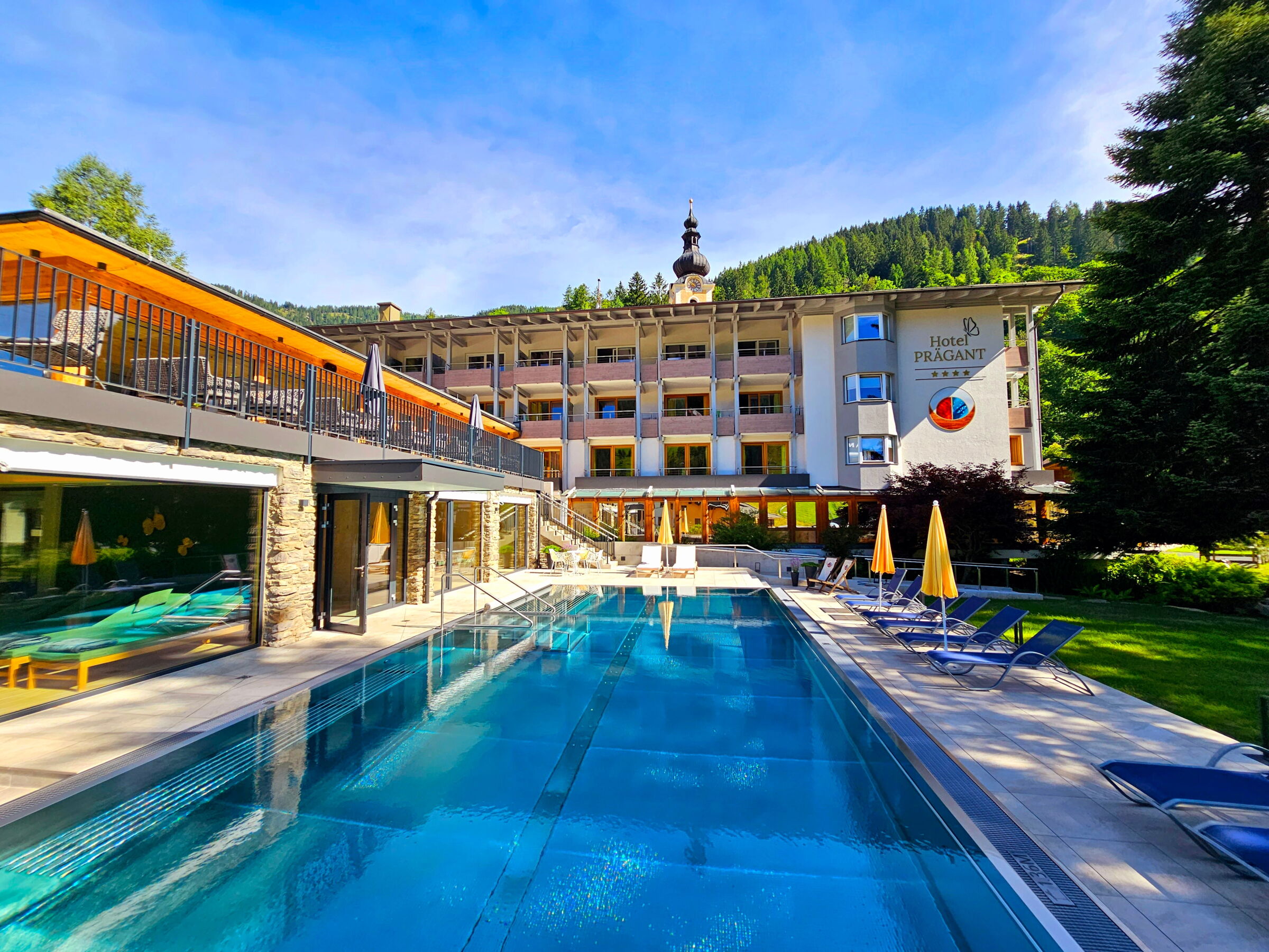 Hotel mit Schwimmbad inmitten von Bergen und Grünflächen umgeben von Natur, ideal für Erholung.