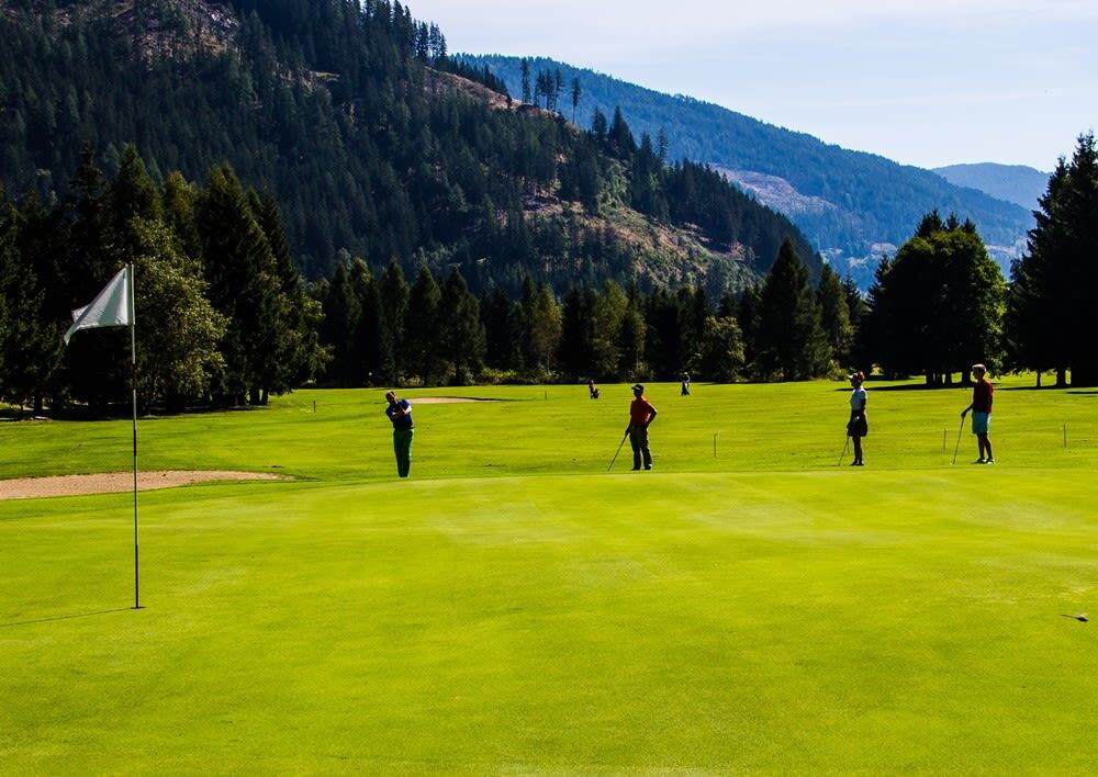 Golfplatz mit mehreren Golfern und umliegender Natur, einschließlich Bäume und Berge im Hintergrund
