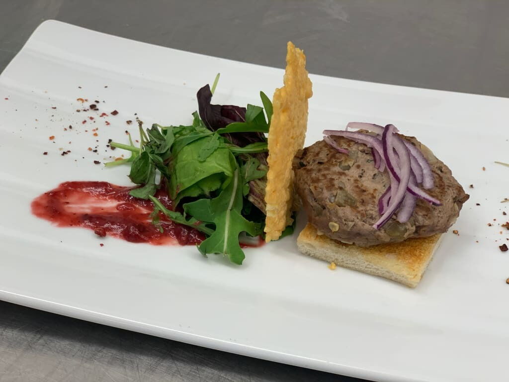 Hochwertiges Gourmetgericht mit einem Fleischpatty auf Toast, begleitet von Salat und Sauce