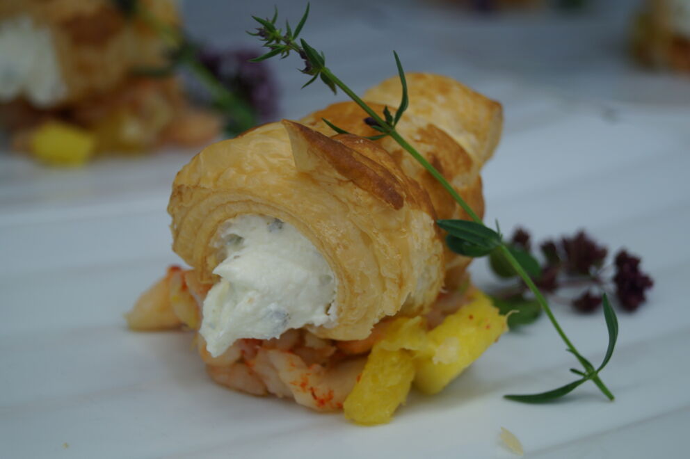Gourmetgebäck mit Sahnefüllung und frischen Kräutern auf einem weißen Teller angerichtet