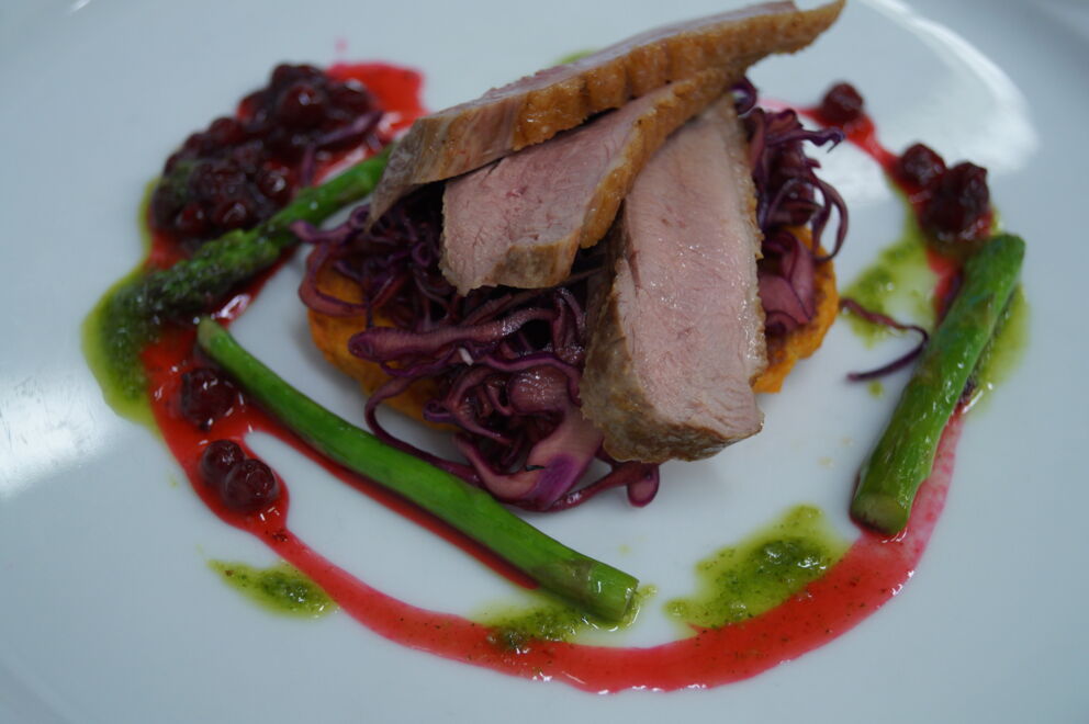 Gourmetgericht mit geschnittenem Fleisch, Rotkohl und Spargel auf dem Teller, verfeinert mit Beerensoße.