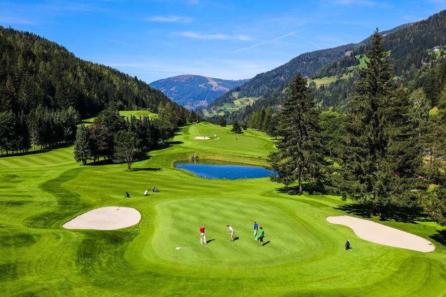 Golfer auf einem malerischen Golfplatz vor einer Berglandschaft mit Teich und Bäumen