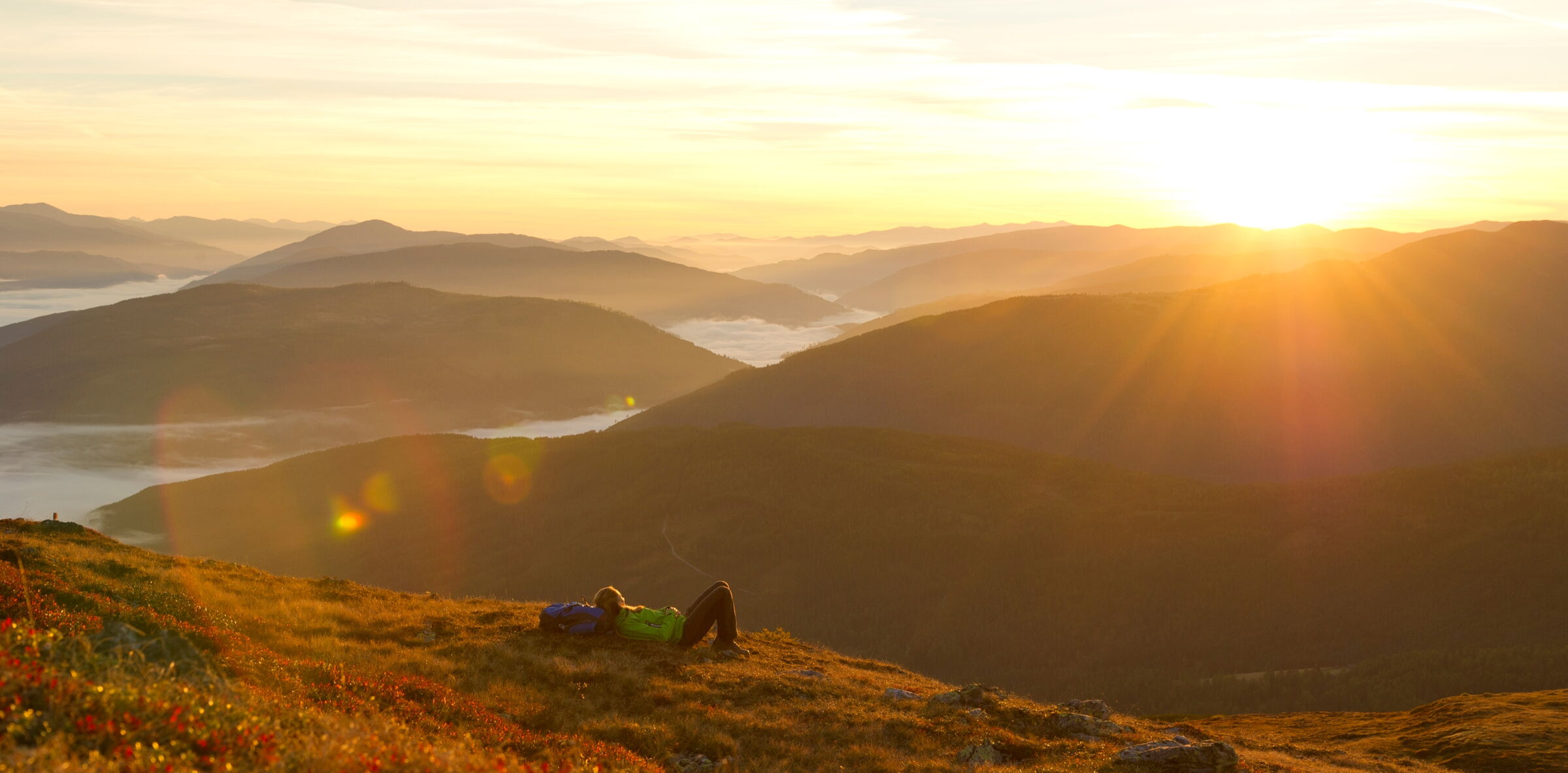 Una donna sdraiata in un prato alpino, che si gode il tramonto in montagna