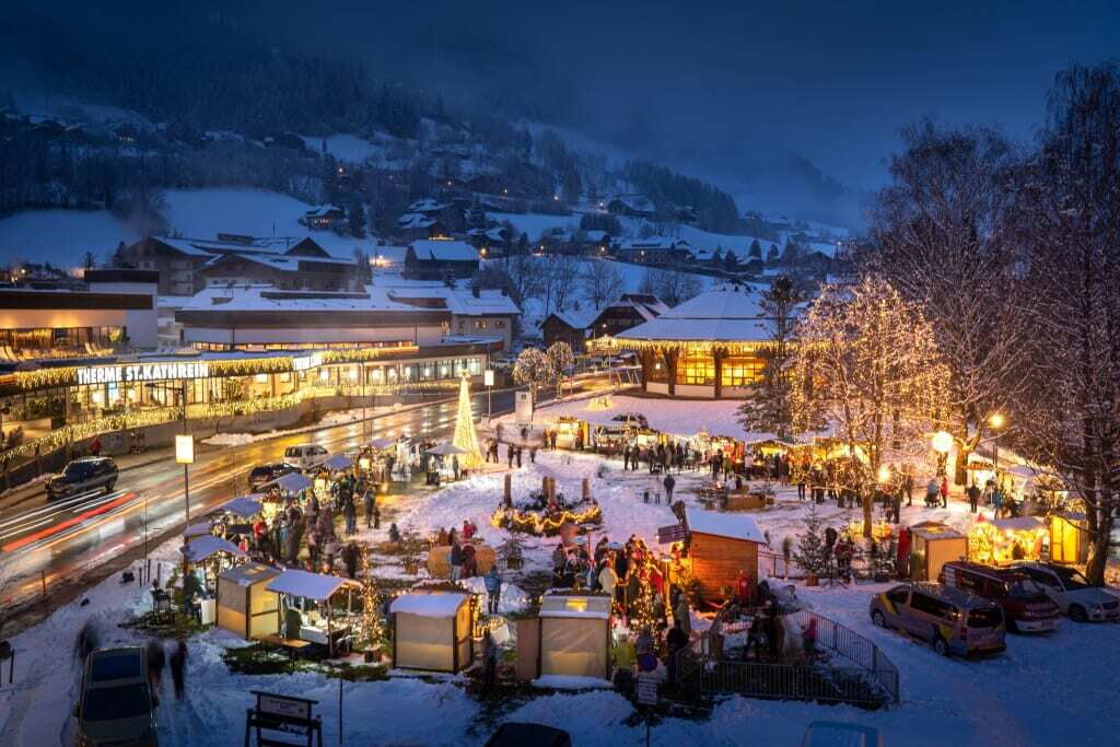 Bunte Lichter und festliche Stände auf einem Weihnachtsmarkt im Schnee mit Menschen beim Shoppen