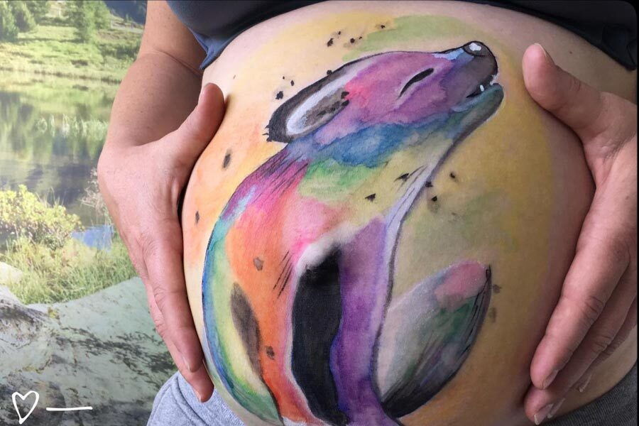 A baby bump with a small colourful wolf painted on it.