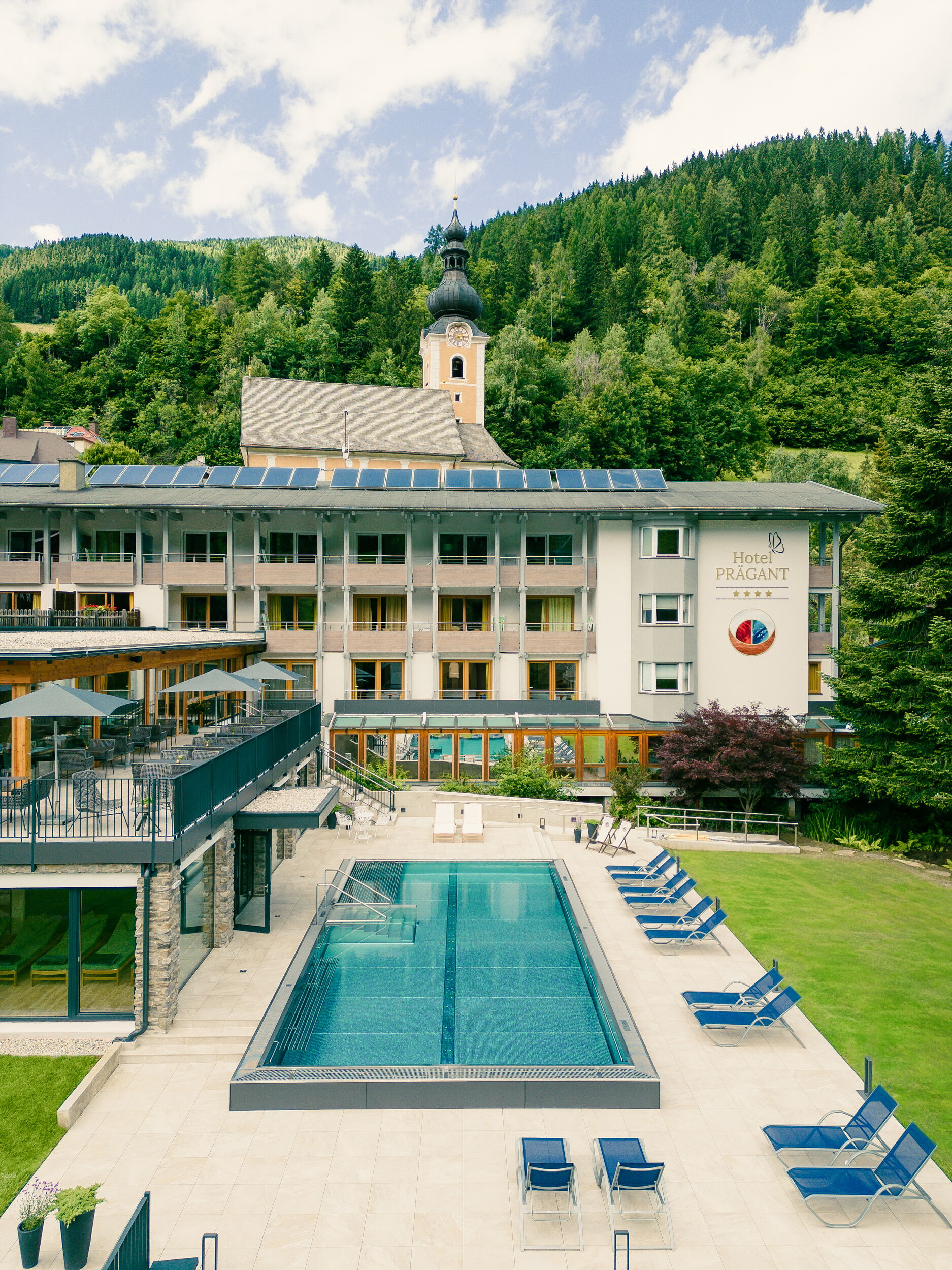Vista della piscina all'aperto dell'Hotel Prägant e della facciata esterna dell'albergo