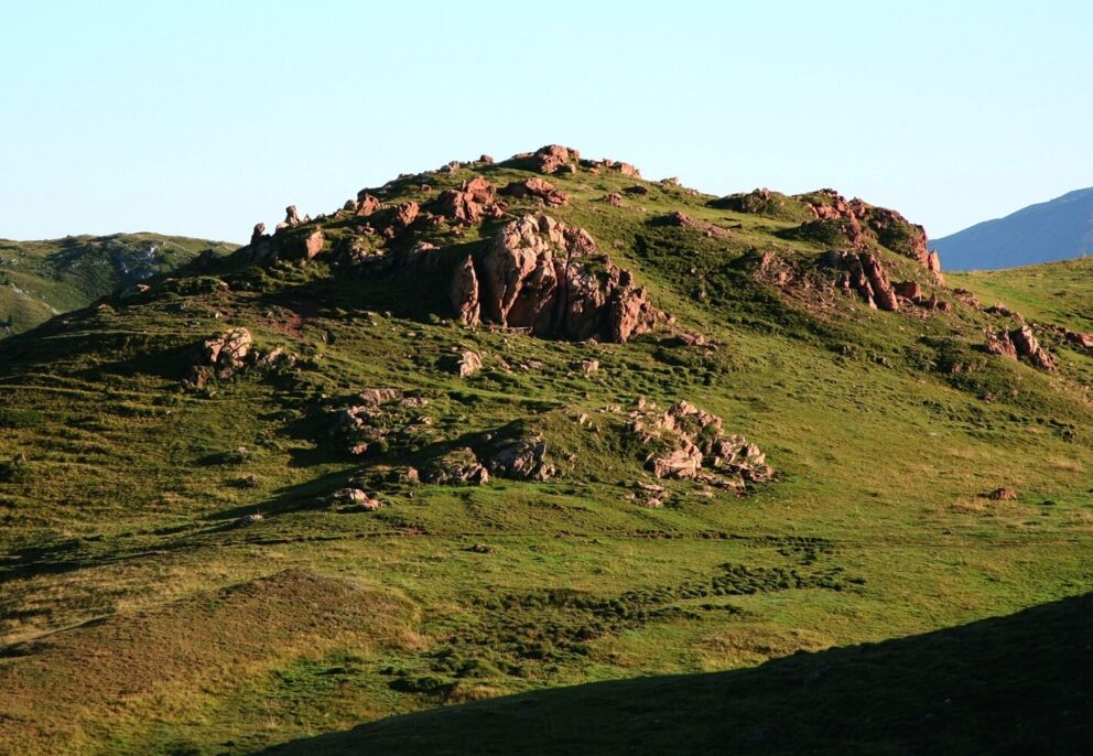 Friedliche Landschaft mit einem felsigen Hügel und grünem Gras unter klarem Himmel