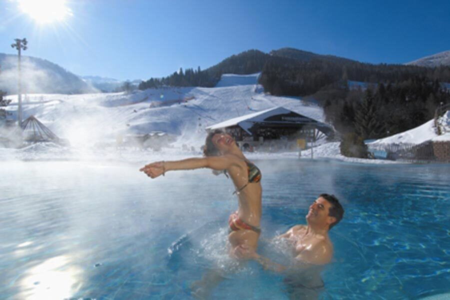 A man and a woman in an outdoor pool at a thermal spa right next to the ski slope