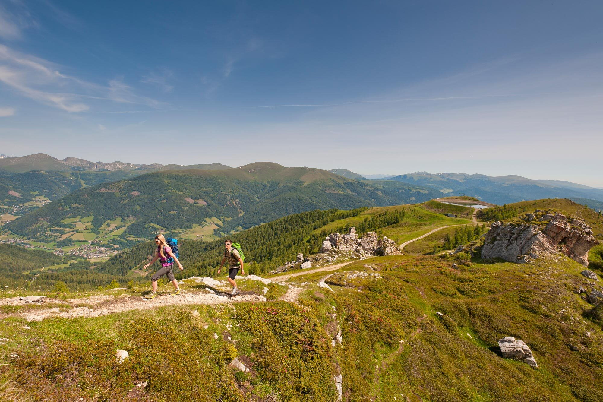 Zwei Wanderer gehen auf einem steinigen Pfad durch die Berge umgeben von Natur und grüner Vegetation
