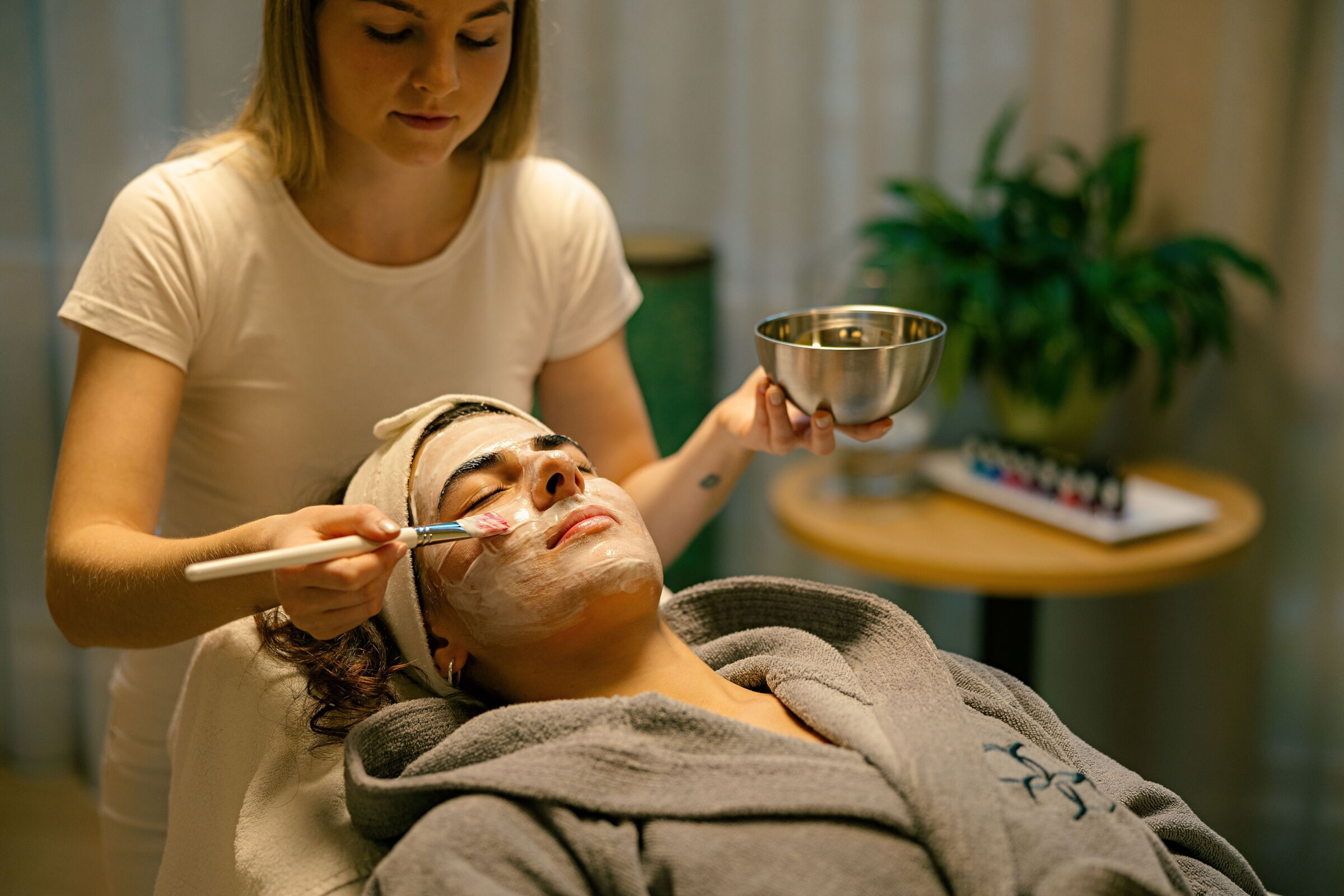 Therapeut trägt einer liegenden Person eine Gesichtsmaske auf während einer Spa-Behandlung.