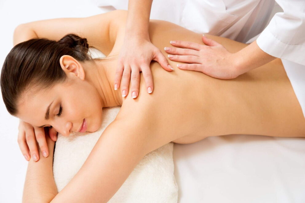 Eine Frau liegt auf einem Massagetisch und erhält eine Rückenmassage von einer Therapeutin.