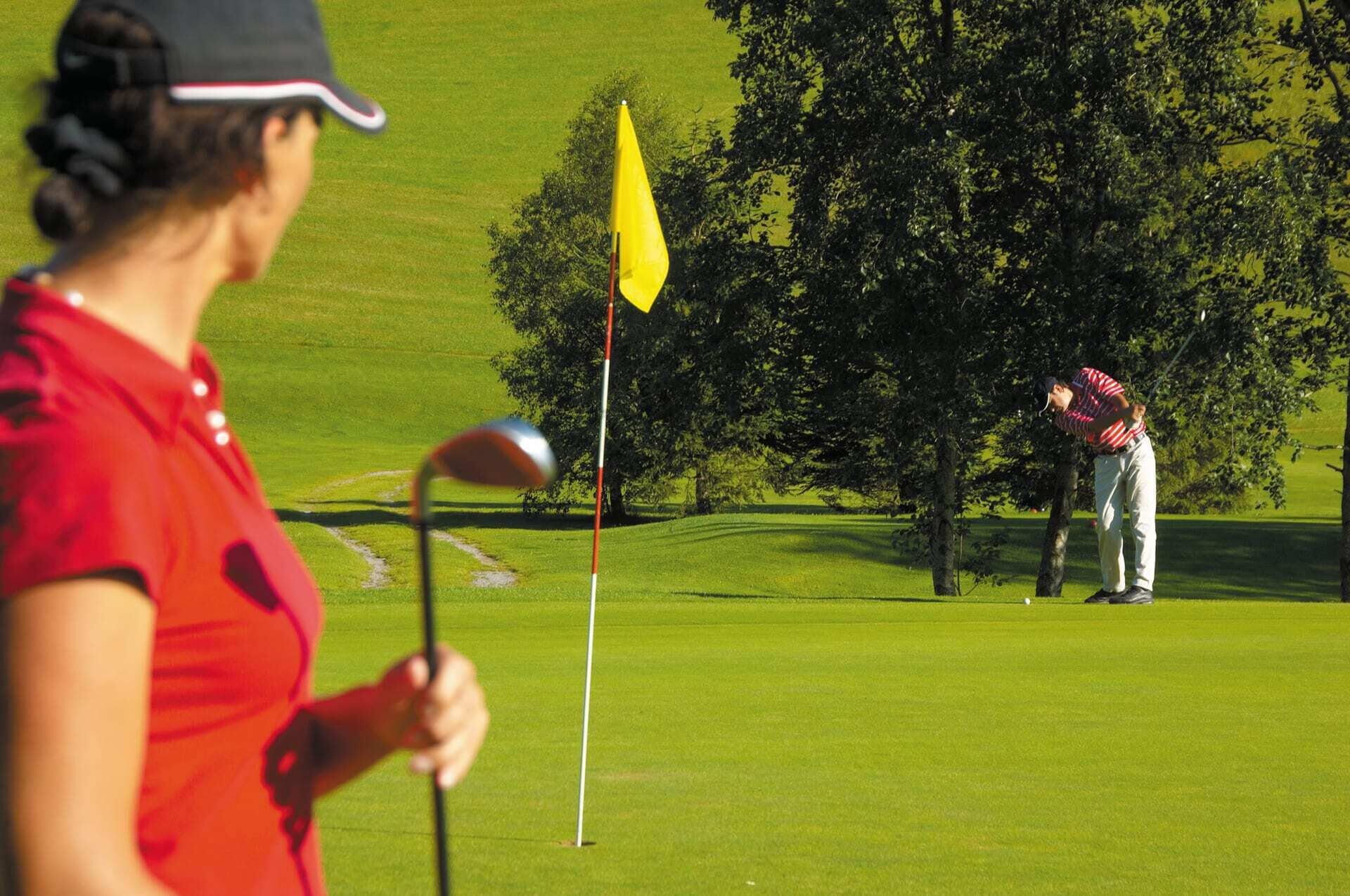 Eine Golferin hält ihren Schläger während ein männlicher Golfer auf dem Putting Green ist