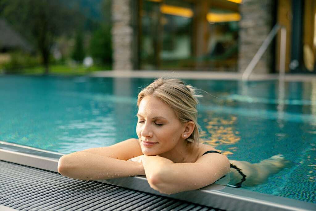 Frau entspannt am Rand eines Schwimmbeckens in einer ruhigen Umgebung mit geschlossenen Augen