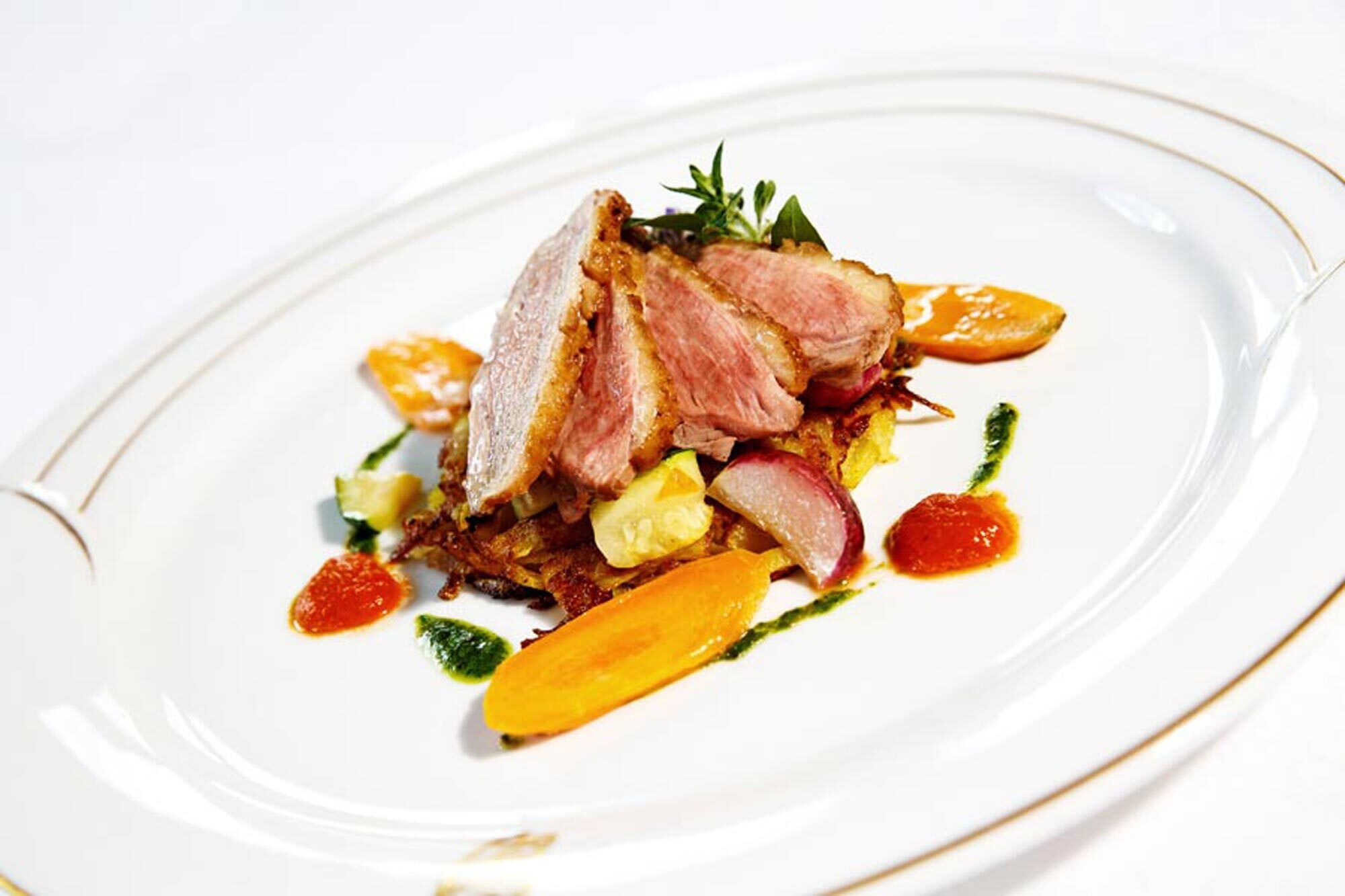 Ein kunstvoll angerichtetes Gourmetgericht mit Fleisch und Beilagen auf einem Teller.
