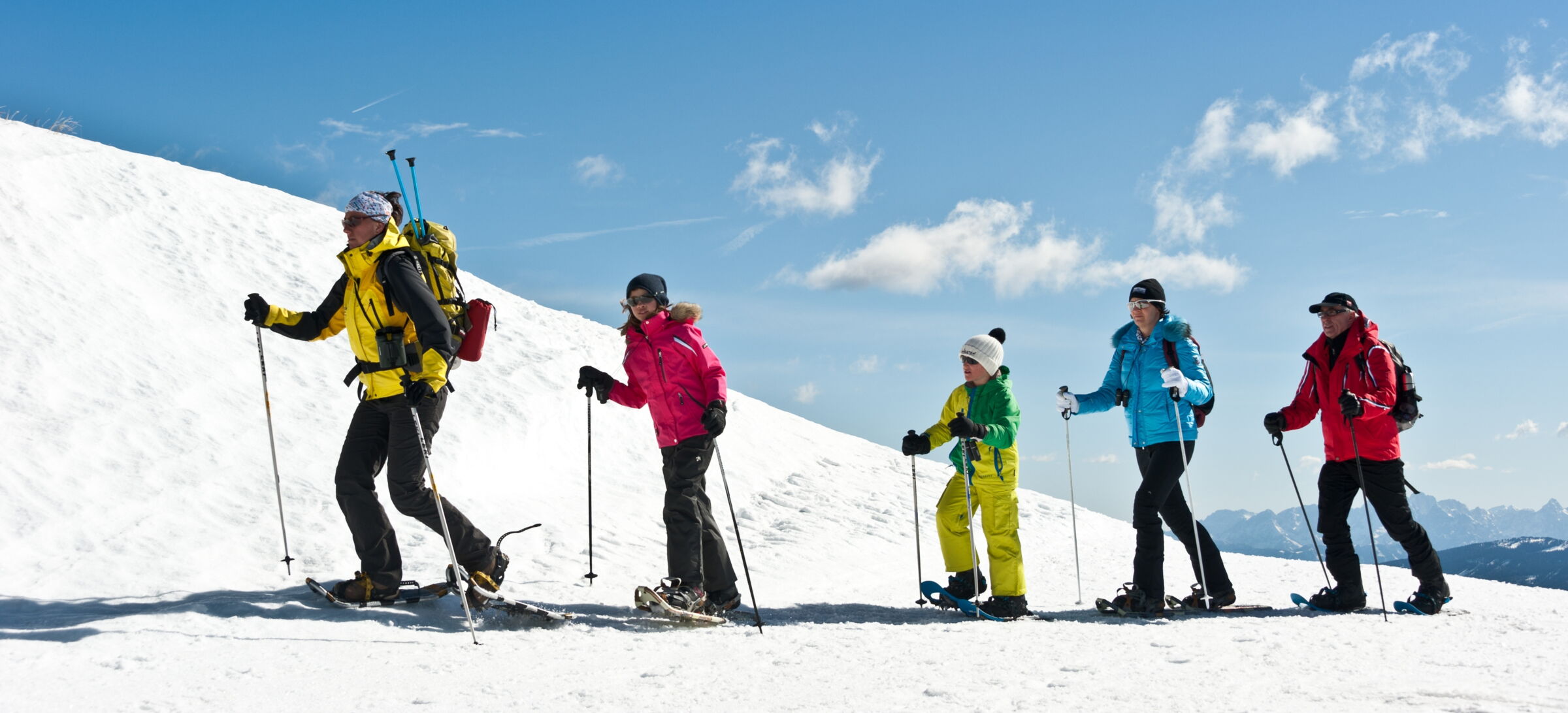 Gruppe von fünf Personen beim Schneeschuhwandern in den Bergen unter blauem Himmel.