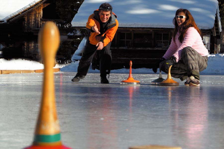 Zwei Personen spielen Curling auf einer Eisfläche mit Fokus auf den Curlingsteinen