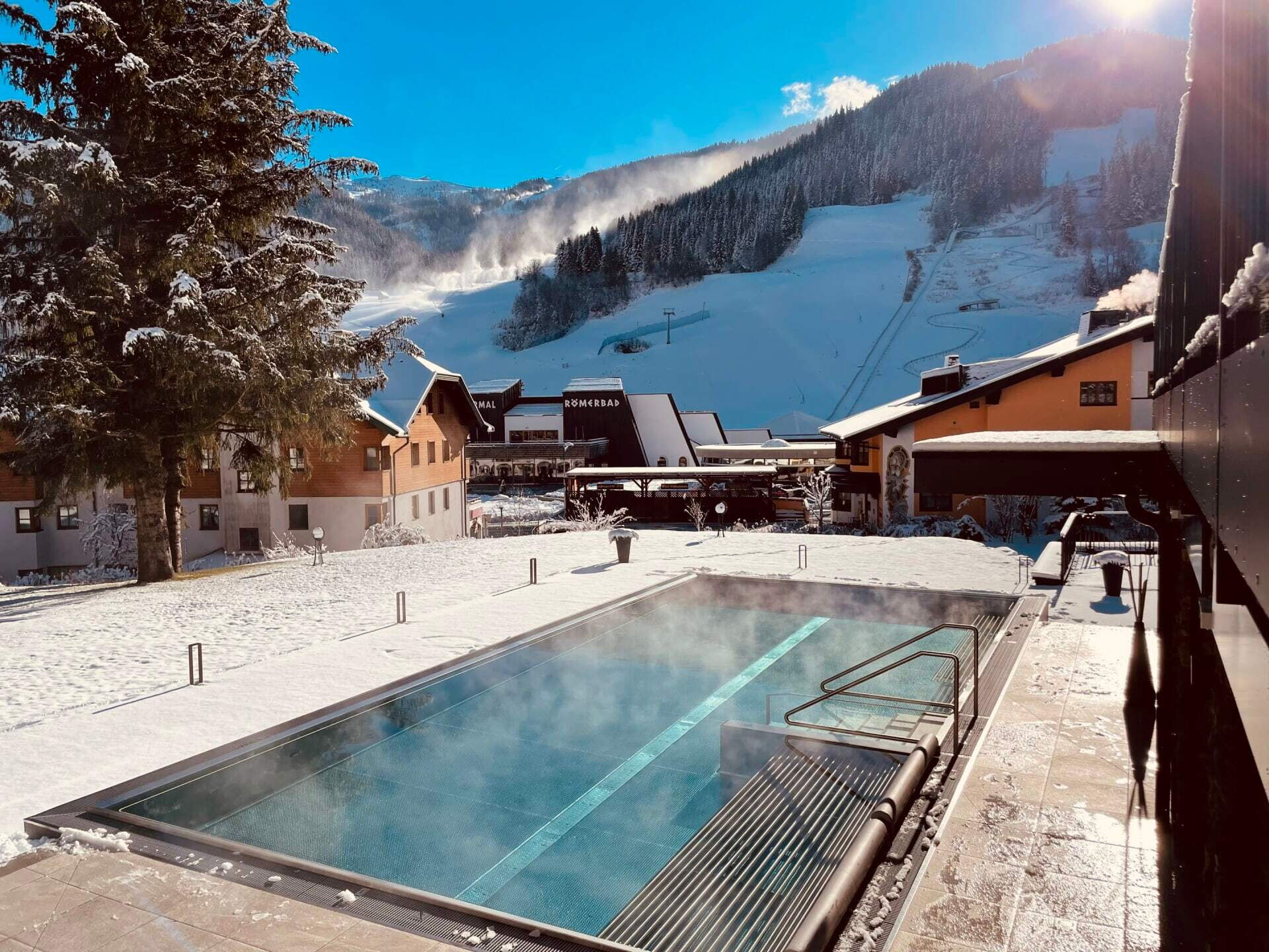 Außenpool umgeben von Schnee mit Berglandschaft im Hintergrund und Resortgebäuden