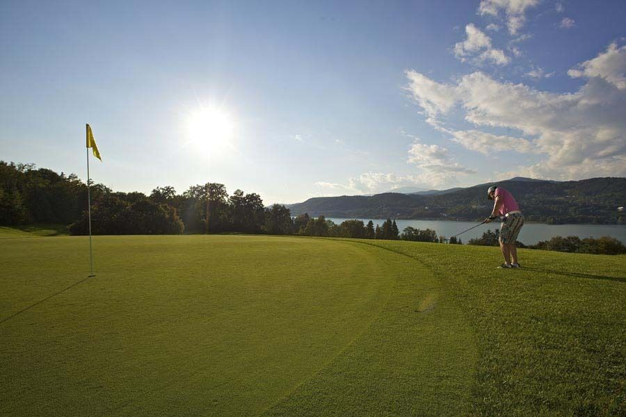 Golfer puttet auf einem gepflegten Golfplatz mit Blick auf Hügel und einen See unter klarem Himmel.
