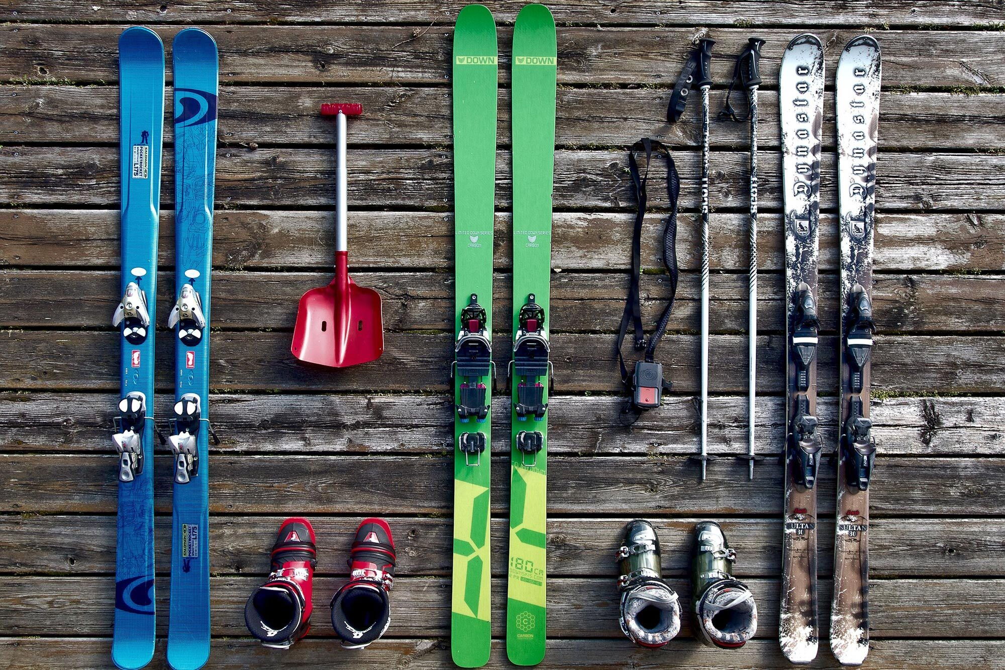 Verschiedene Skiausrüstungen wie Ski, Stöcke und Boots auf einer Holzoberfläche.