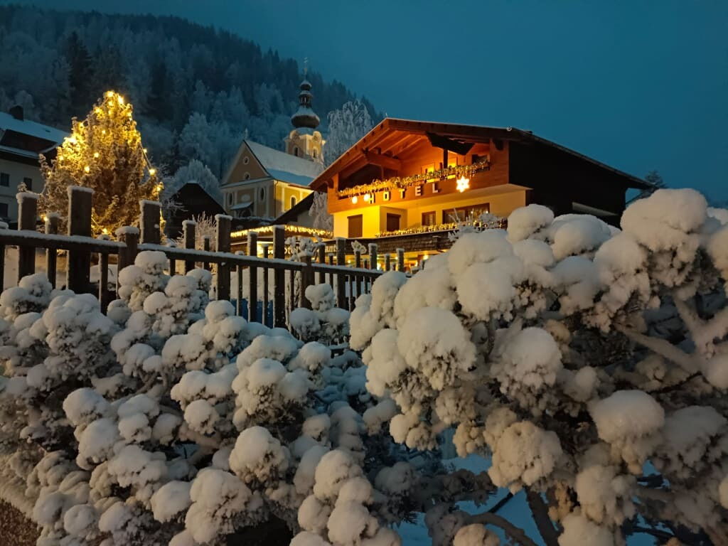 Hotel mit festlichen Lichtern umgeben von schneebedeckten Bäumen und Bergen im Hintergrund
